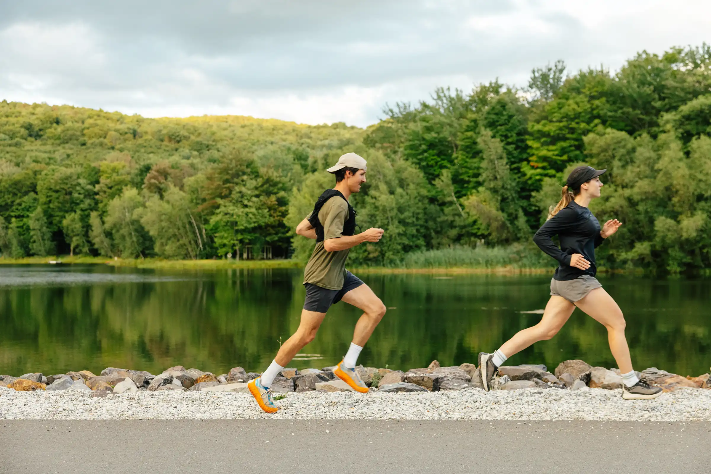 Deux coureurs sur un chemin de gravier au bord d'un lac, collines boisées à l'horizon