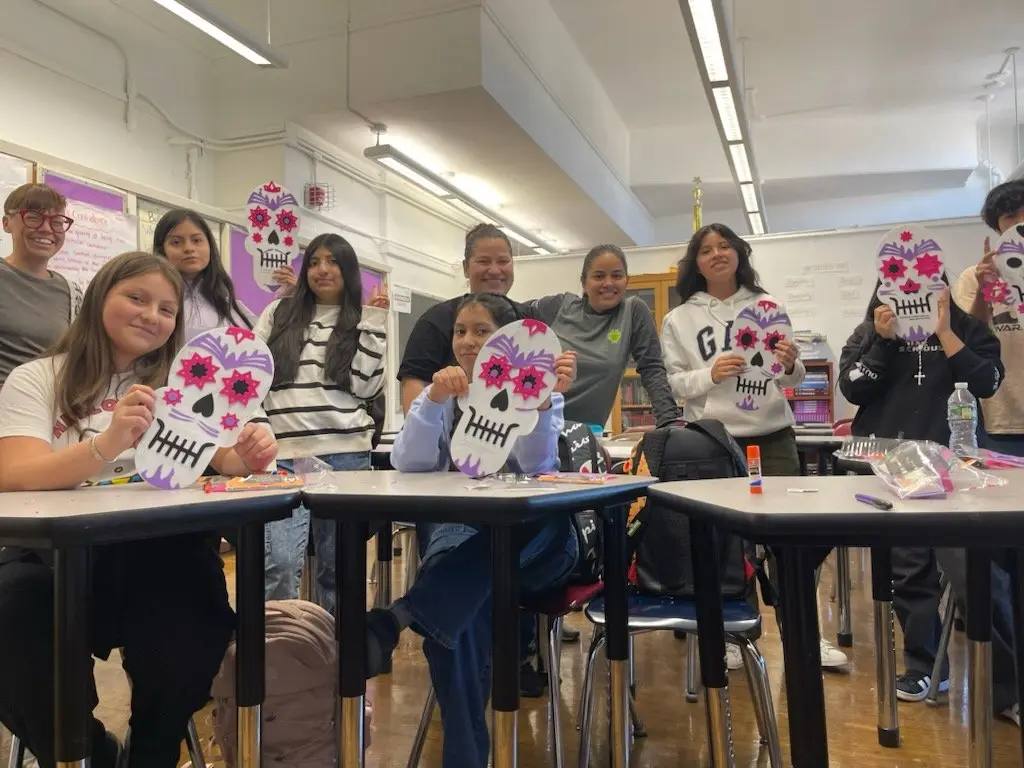Students and teacher displaying handmade Día de los Muertos sugar skull crafts