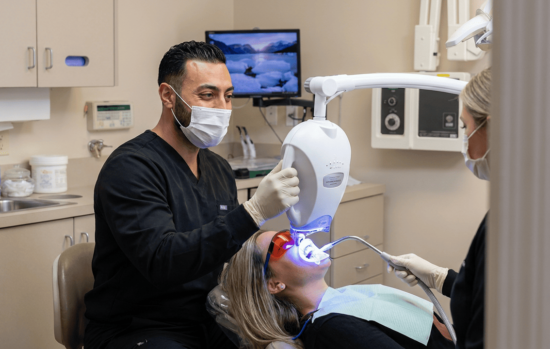 Dentist Dr. Khaddor applies an LED whitening lamp to a patient's teeth during an in-office whitening procedure.