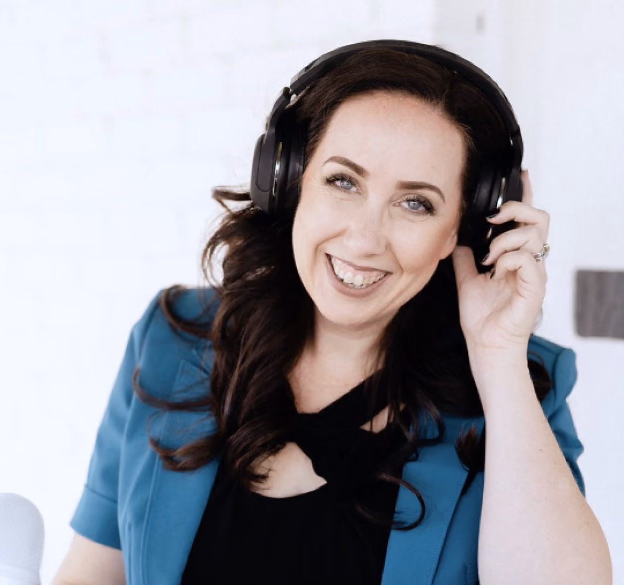 Smiling woman with long dark hair wearing a blue blazer and black headphones, holding one side of the headphones.