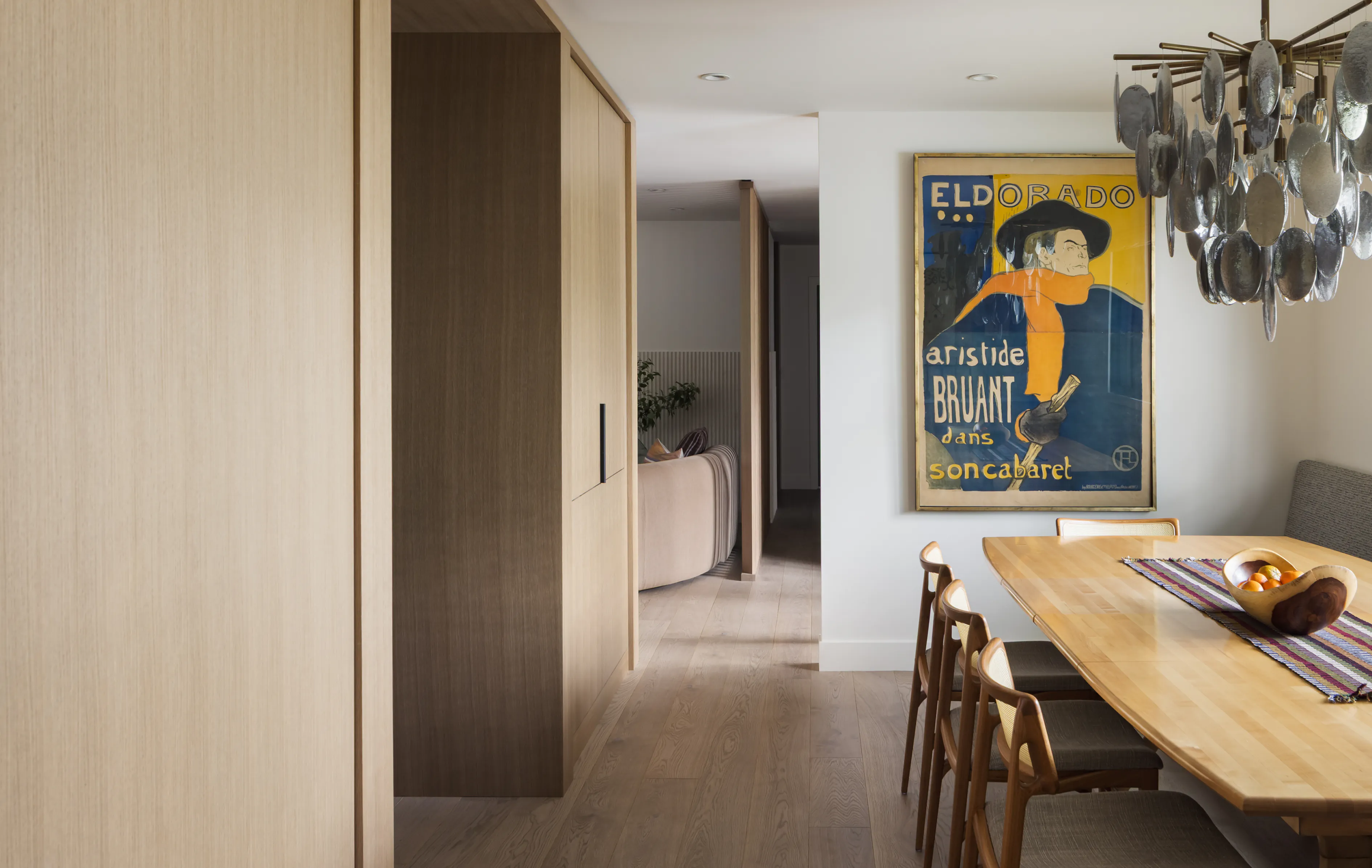 Modern dining area with wooden table, chairs, artistic wall poster, and unique metal chandelier.