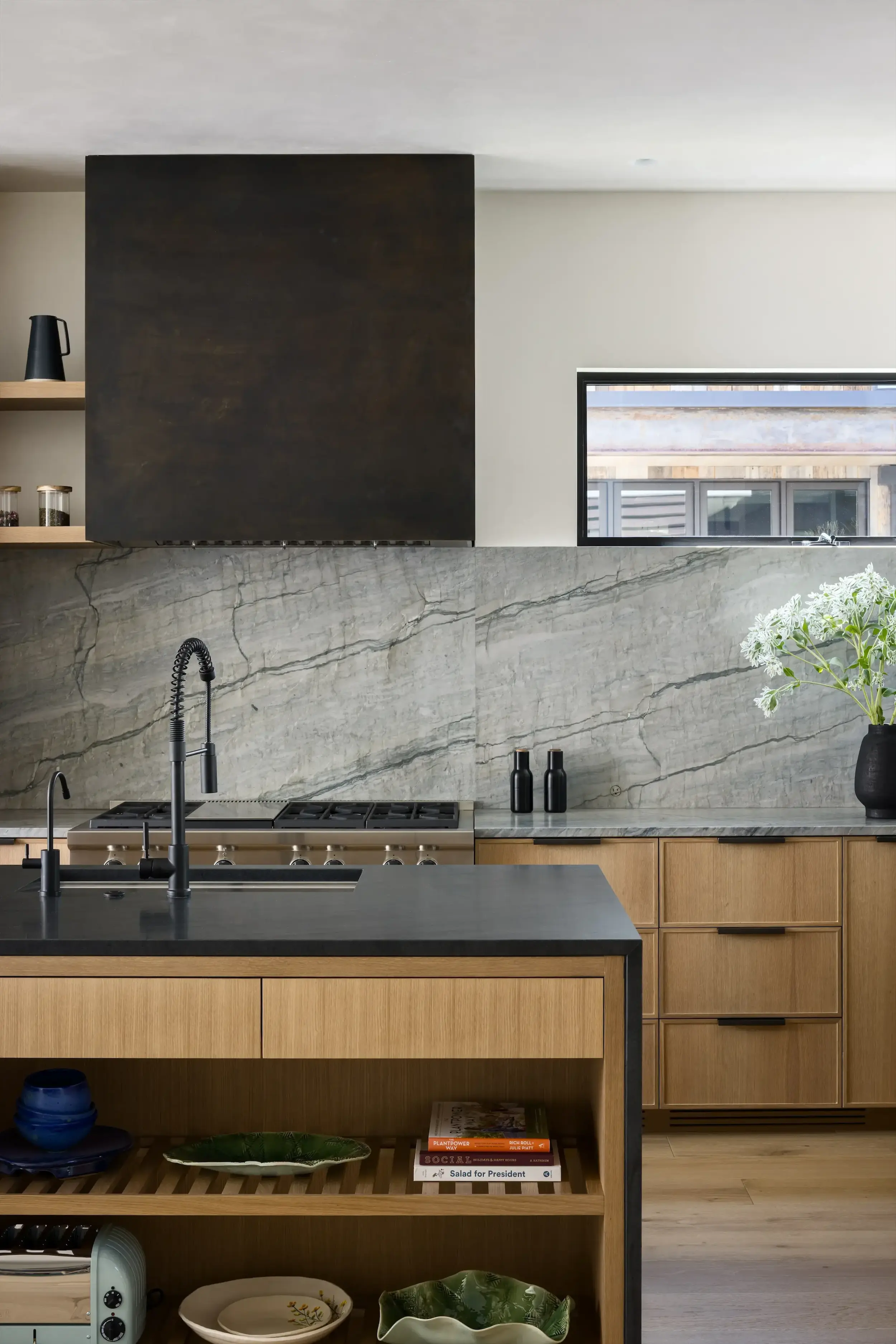 Modern kitchen with wooden cabinets, black countertop island, gray marble backsplash, and a window.