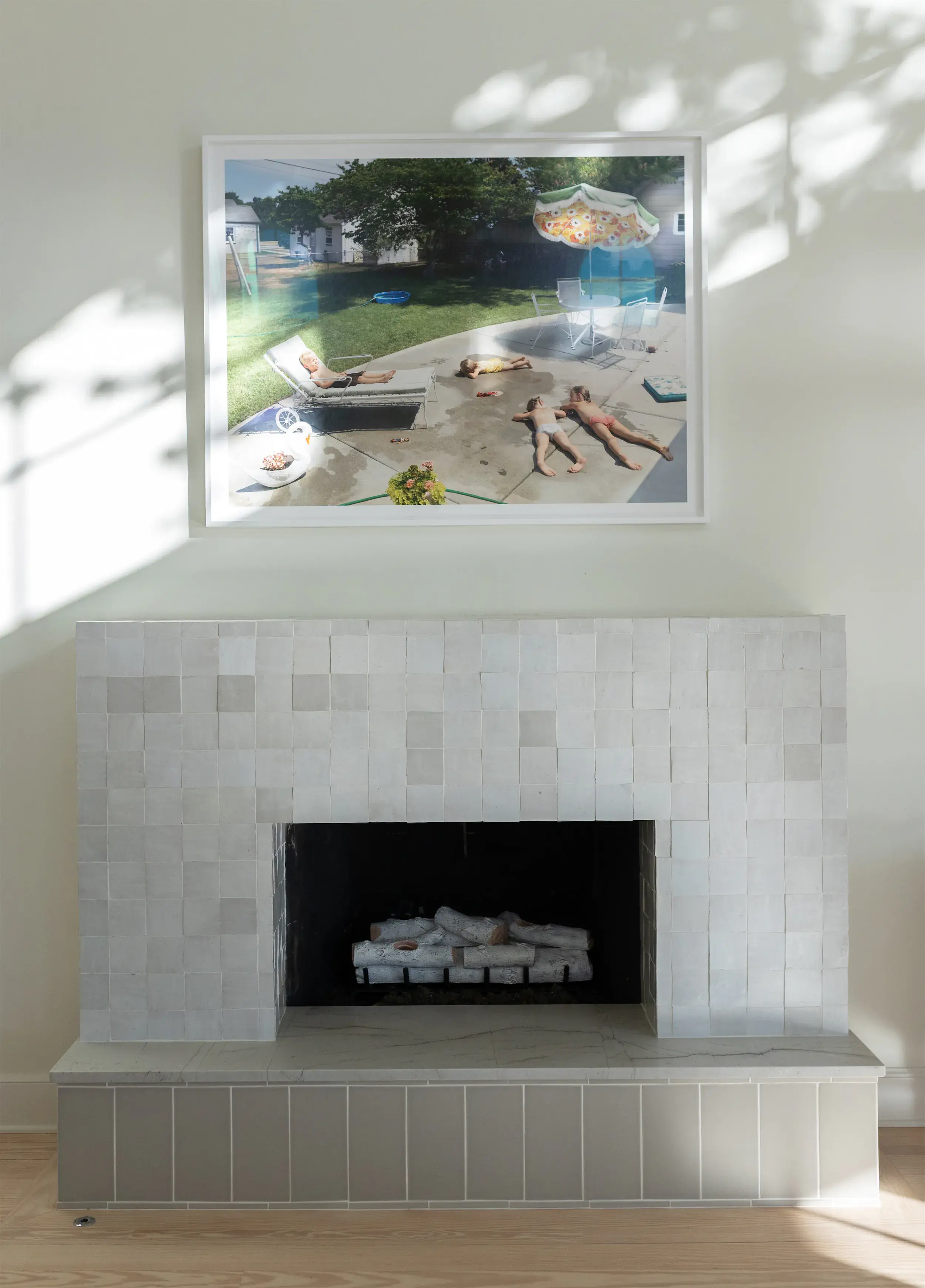 Modern white tiled fireplace with a framed photo of children lying on a patio hanging above it.