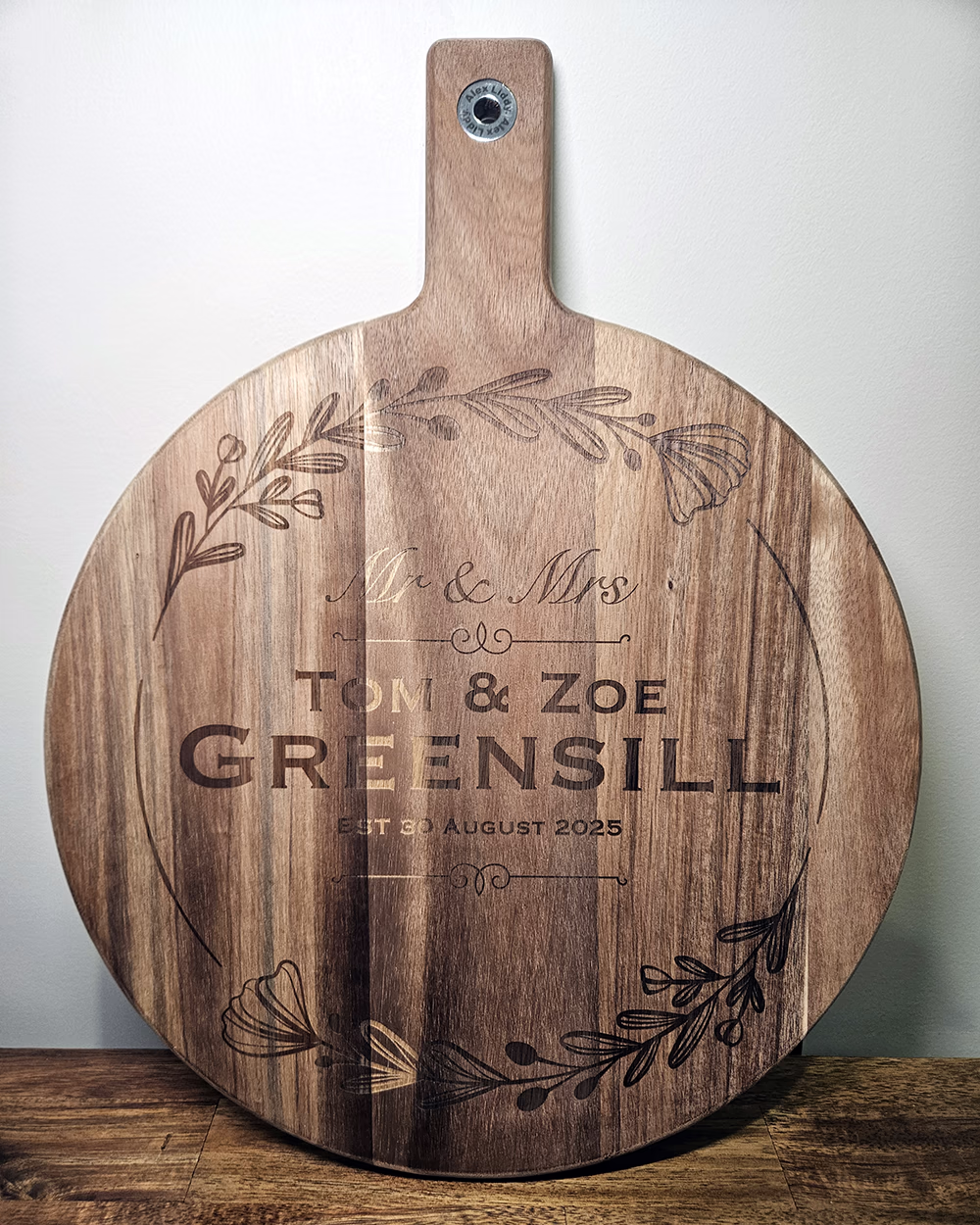 Round timber paddle board engraved Mr and Mrs Tom and Zoe Greensill with the wedding date and a floral wreath