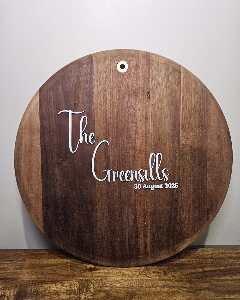 Round dark timber signing board engraved The Greensills, 30 August 2025, for wedding guests to sign