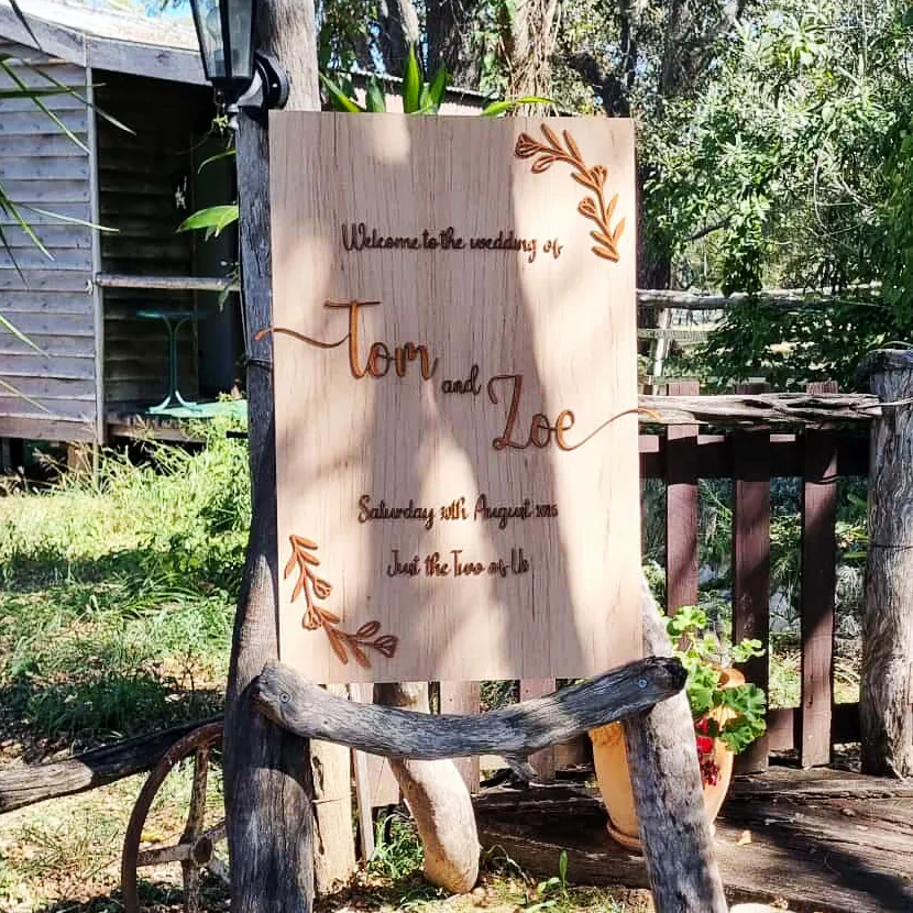 Engraved timber wedding welcome sign for Tom and Zoe set up outdoors on a rustic timber stand