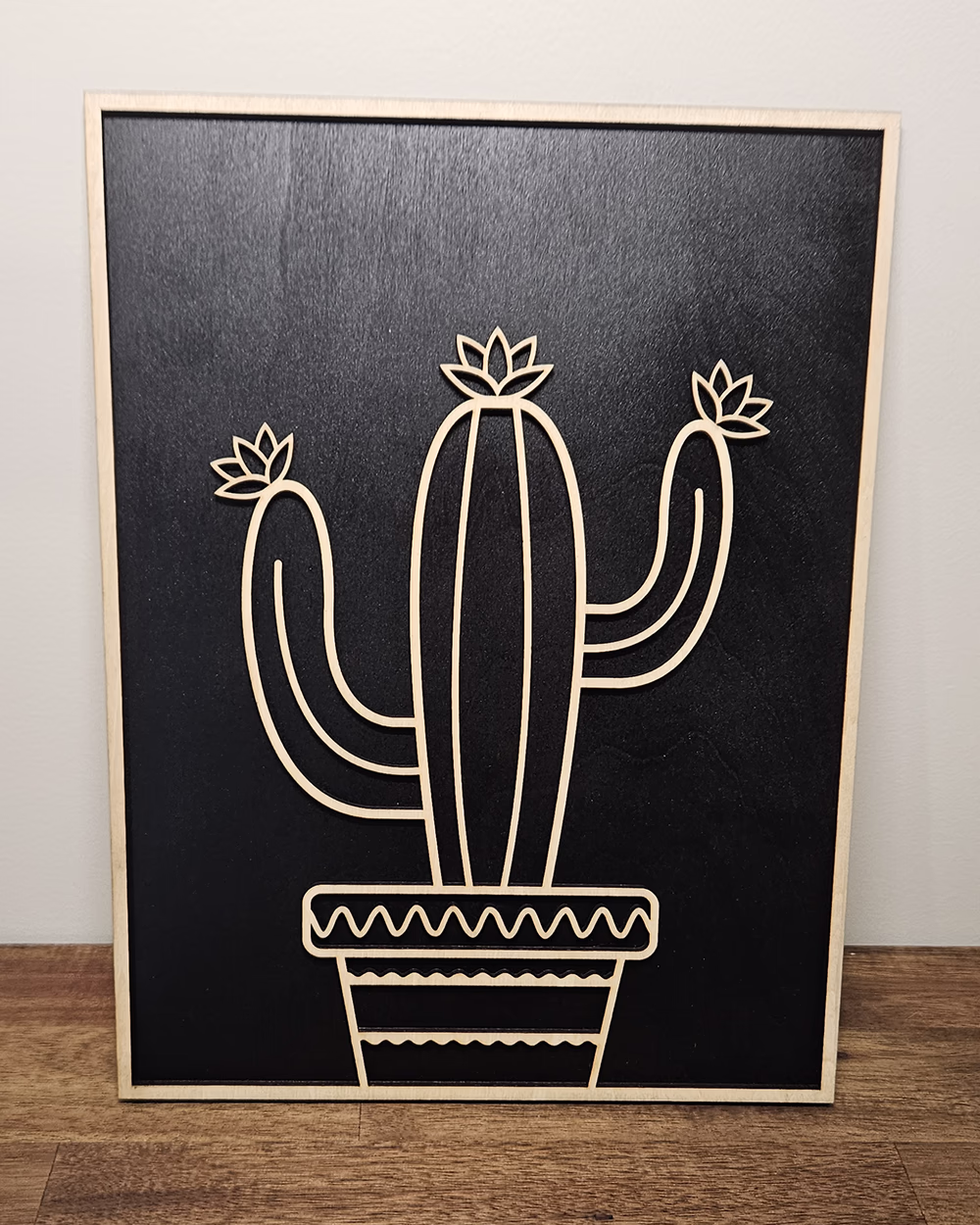 Layered timber wall art of a potted cactus mounted on a black panel