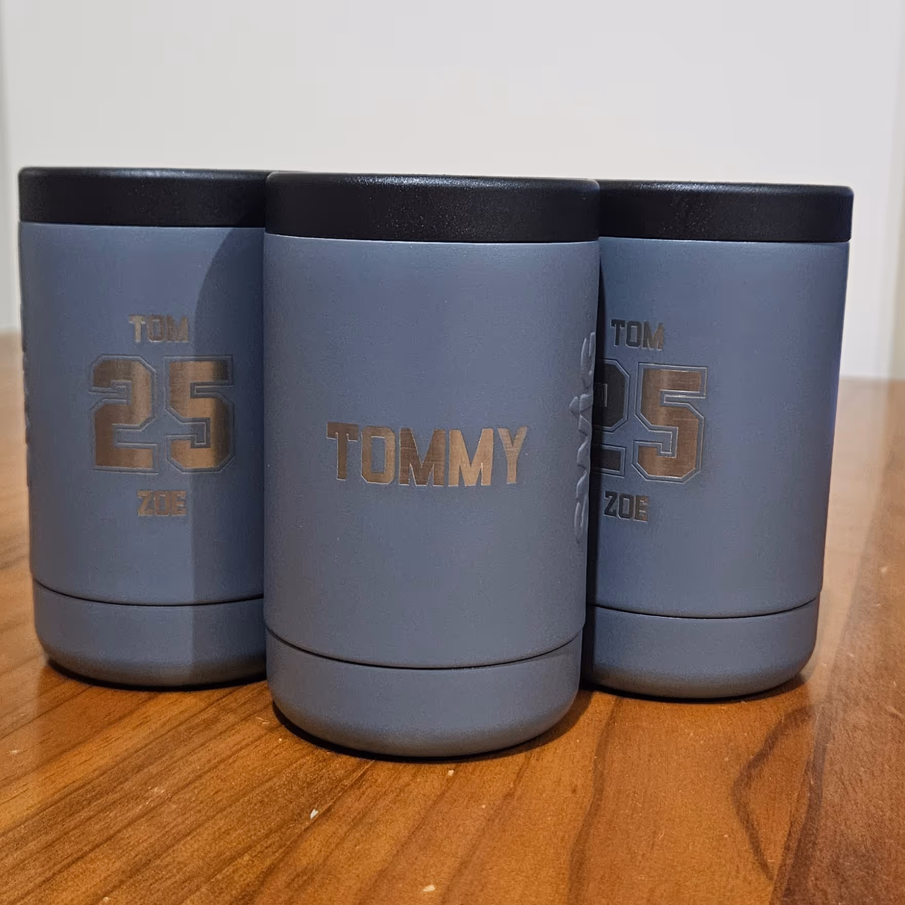 Three grey metal stubby coolers engraved with names and a wedding date