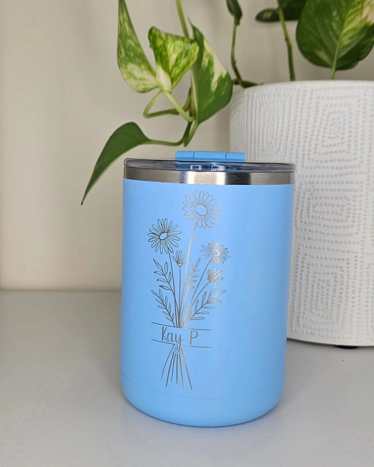 A pale blue tumbler engraved with a wildflower bouquet and a name