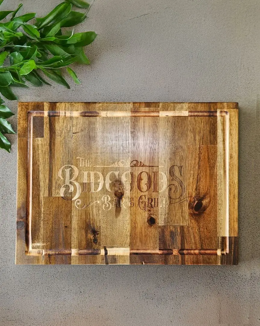 A timber chopping board engraved with a bar and grill business logo