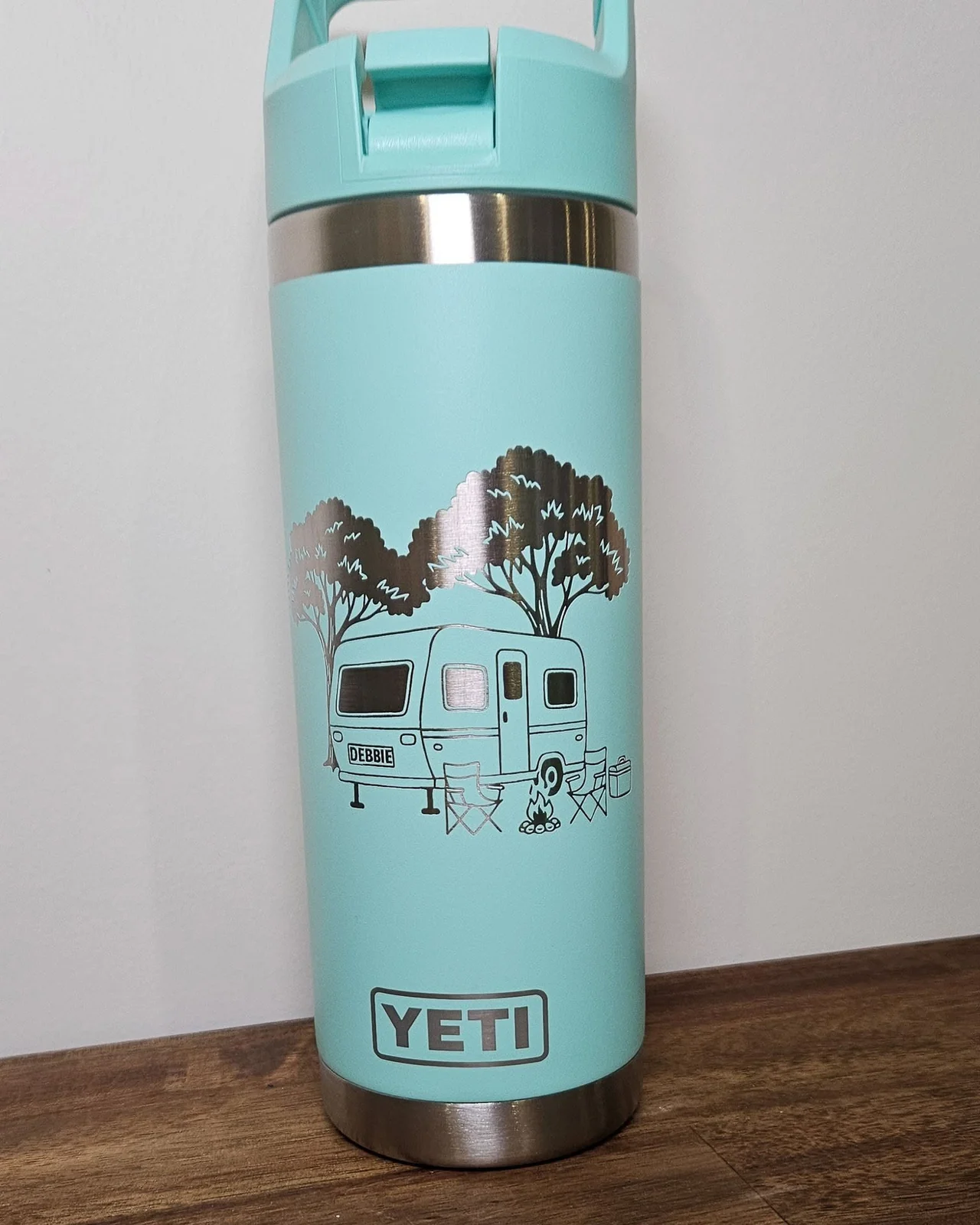 A teal insulated bottle engraved with a caravan and campfire scene