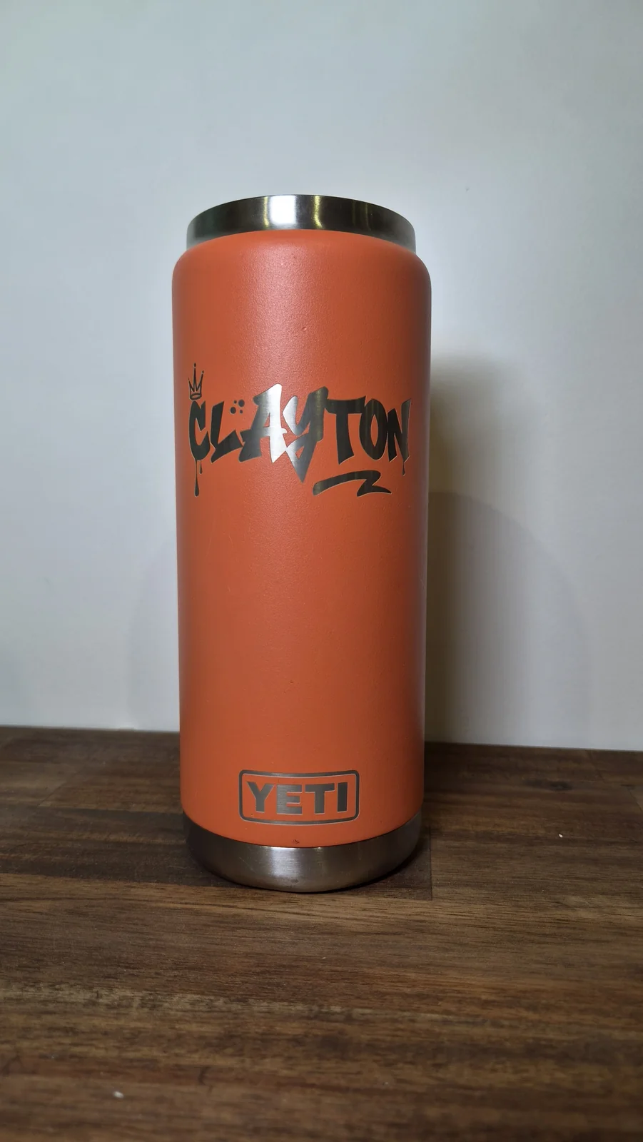A rust-orange insulated bottle engraved with the name Clayton in graffiti lettering