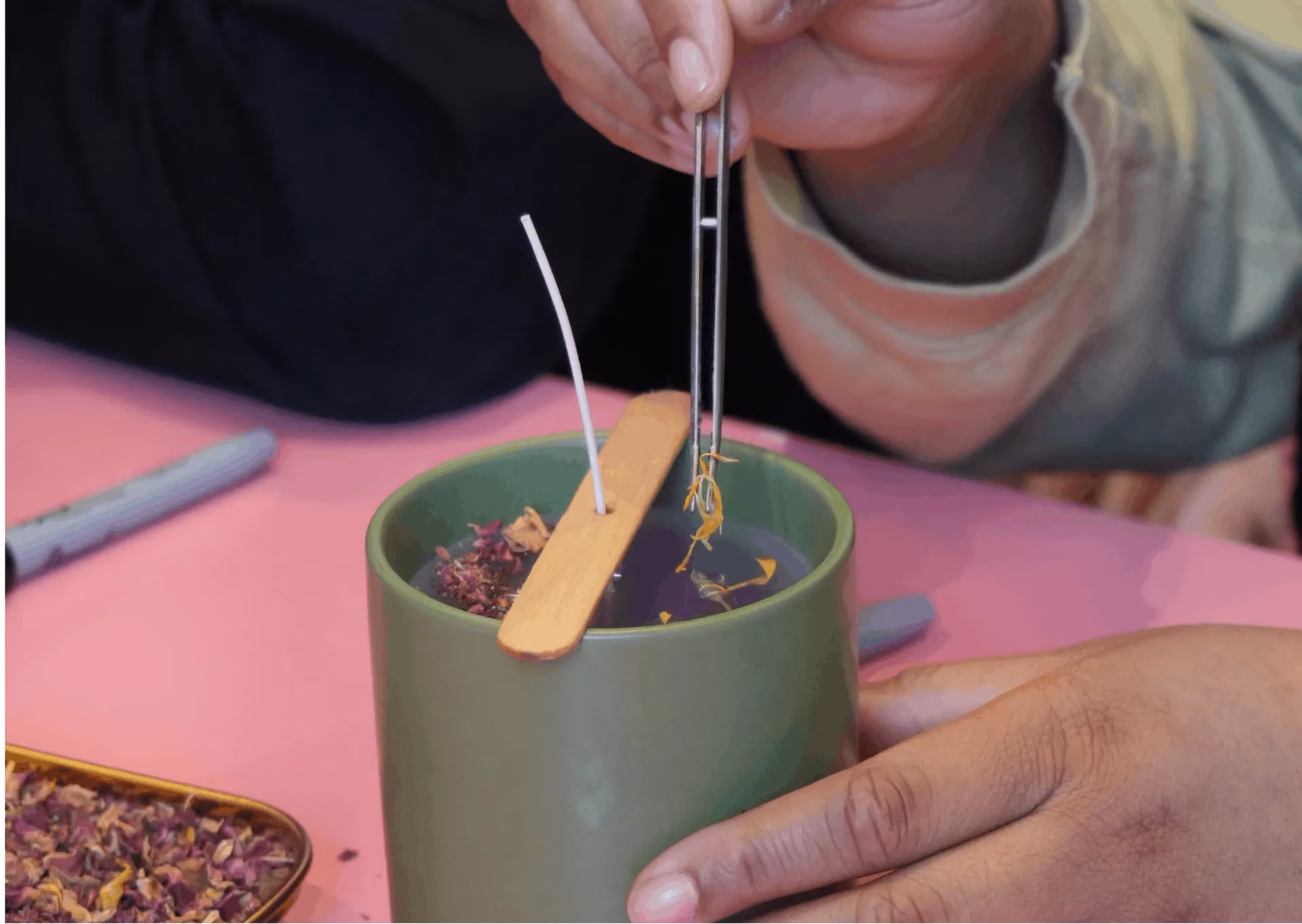Guest placing a wick in a green candle vessel filled with dried botanicals at Wick & Pour