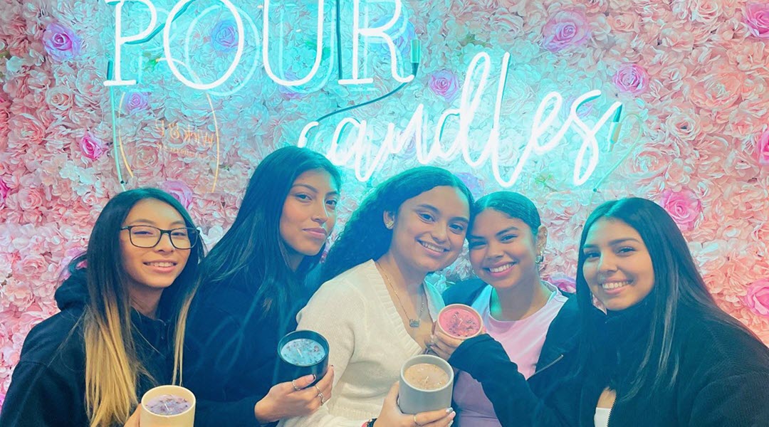 Five friends holding their finished candles under the Pour Candles neon sign at Wick & Pour