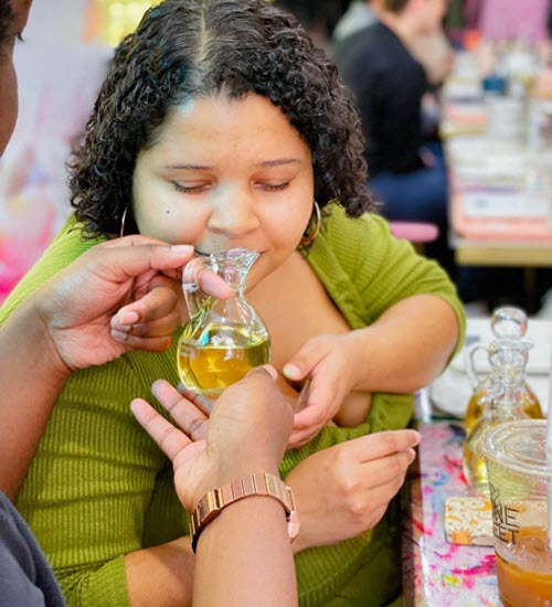 Instructor holding a fragrance bottle for a guest to smell at Wick & Pour