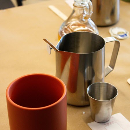 Steel pouring pitcher and red candle vessel ready for a candle making class