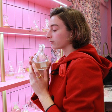 Guest in a red coat smelling a fragrance bottle at the pink shelves of Wick & Pour