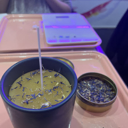 Candle topped with blue cornflower petals beside a tin of dried flowers at Wick & Pour