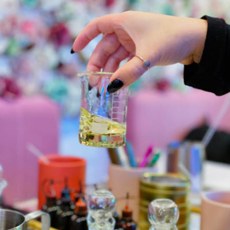 Measuring beaker of fragrance oil held over a Wick & Pour candle making tray