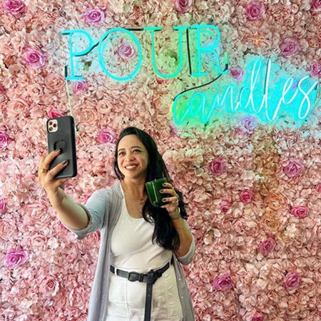Guest taking a selfie with her candle at the Pour Candles neon wall at Wick & Pour