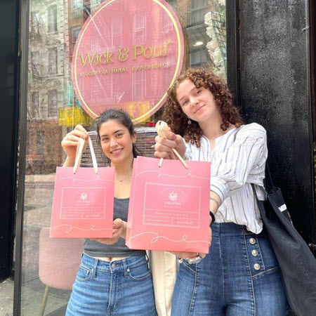 Two friends holding Wick & Pour gift bags outside the studio after a birthday candle making class