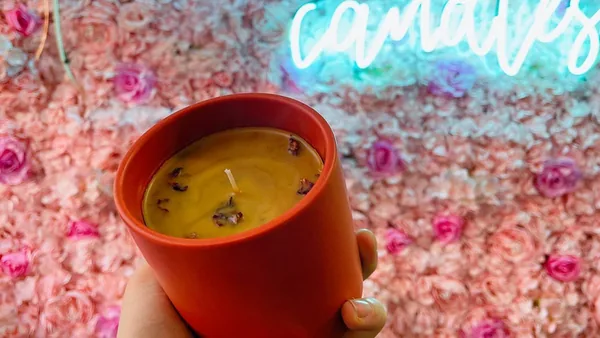 Hand holding a red candle with golden wax in front of Wick & Pour's neon flower wall