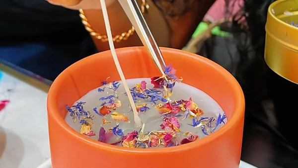 Placing dried flowers on a candle in an orange vessel during a candle making class at Wick & Pour