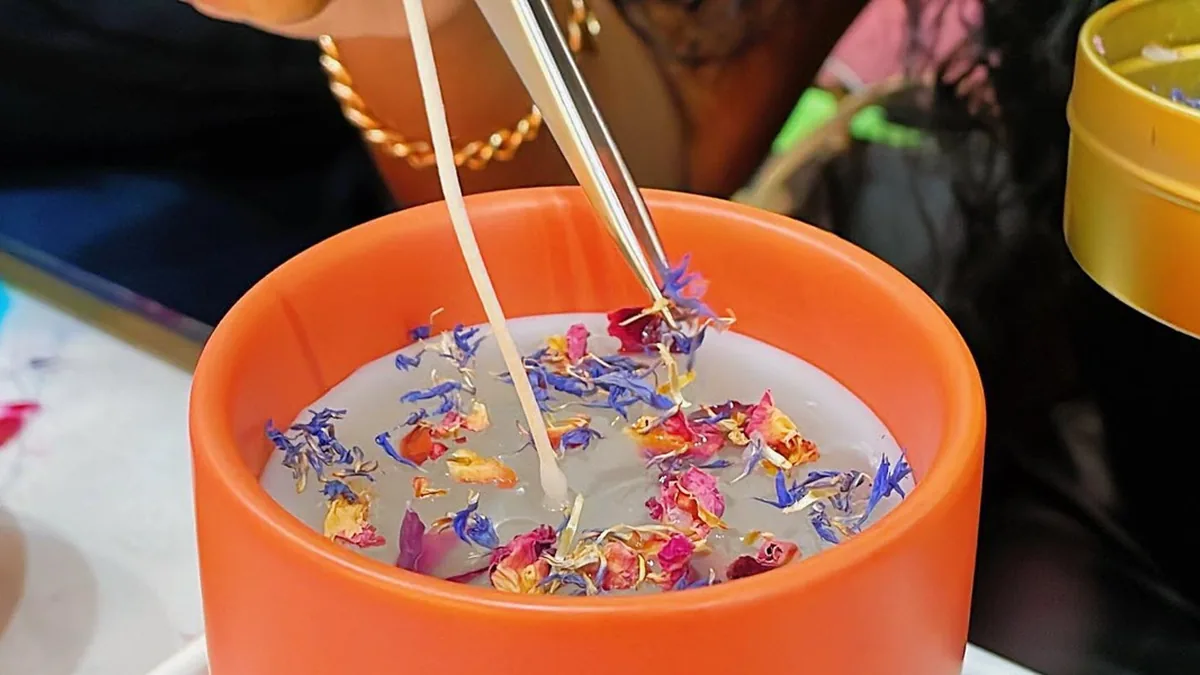 Placing dried flowers on a candle in an orange vessel during a candle making class at Wick & Pour