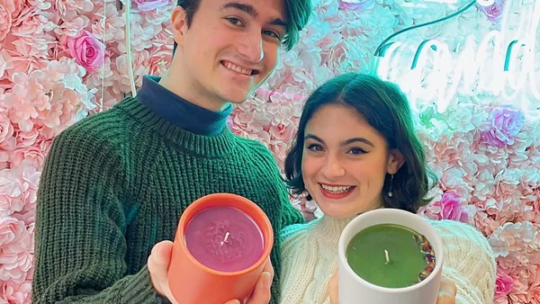 Couple on a date night holding their candles in front of the neon flower wall at Wick & Pour