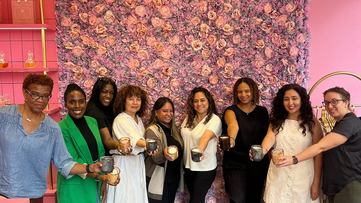 Group of women holding their finished candles in front of a floral wall at Wick & Pour