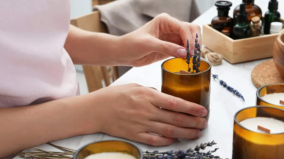 Hands arranging dried lavender in an amber glass candle