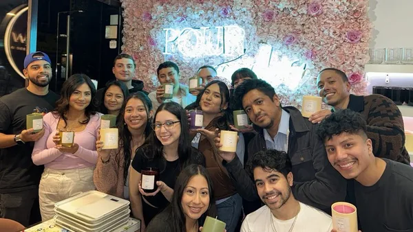 Large group holding their finished candles in front of the neon flower wall at Wick & Pour NYC