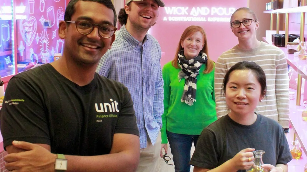Team posing by the neon Wick and Pour sign after a team building candle making class