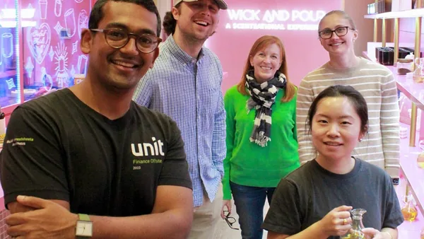 Team posing by the neon Wick and Pour sign after a team building candle making class