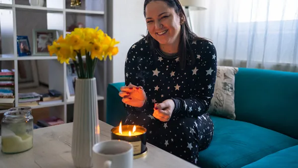 Woman lighting a homemade candle at home beside yellow daffodils