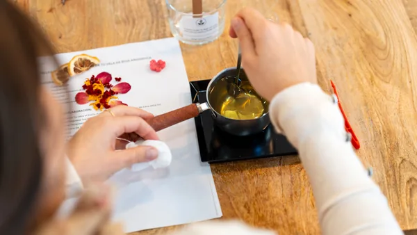 Hands adding fragrance and dried petals to wax during a first candle making class