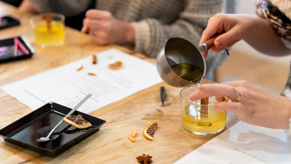 Pouring fragrance oil into a beaker beside dried orange slices and star anise at a candle making class