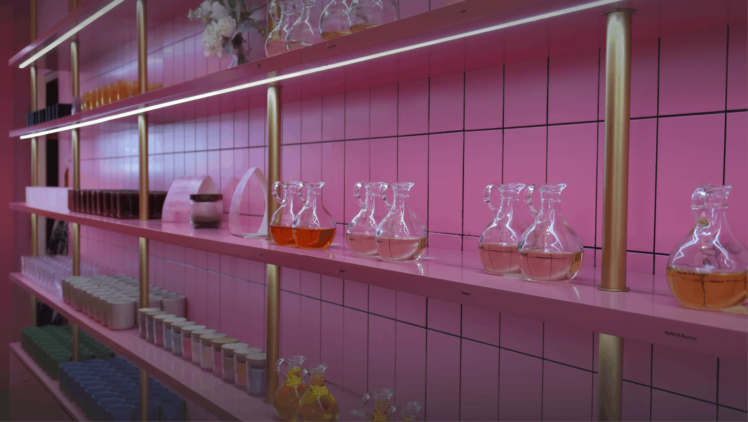 Shelves of glass fragrance decanters on the pink walls of Wick & Pour's NYC candle making studio
