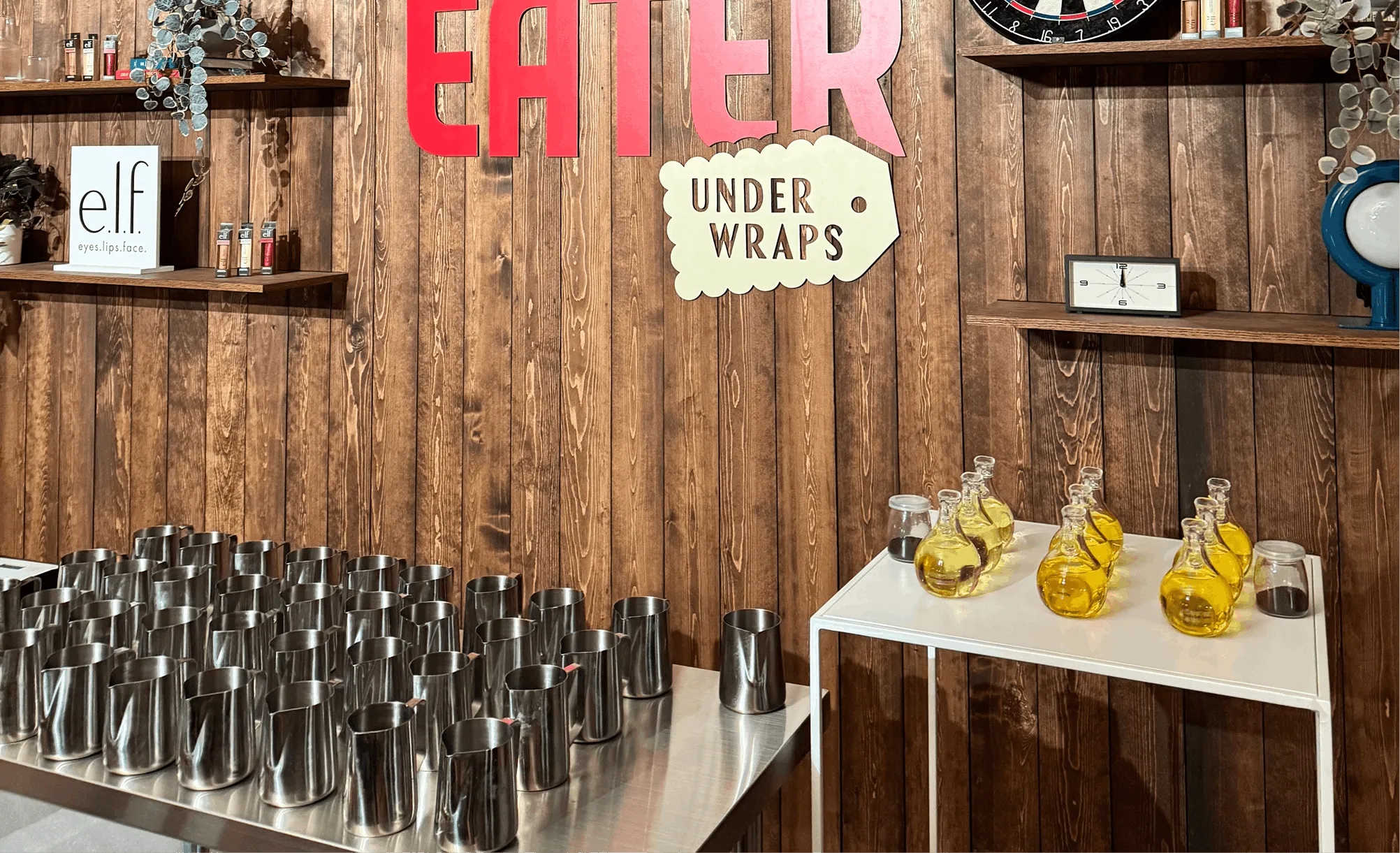 Rows of steel pouring pitchers and fragrance bottles set up for a Wick & Pour corporate event with Eater