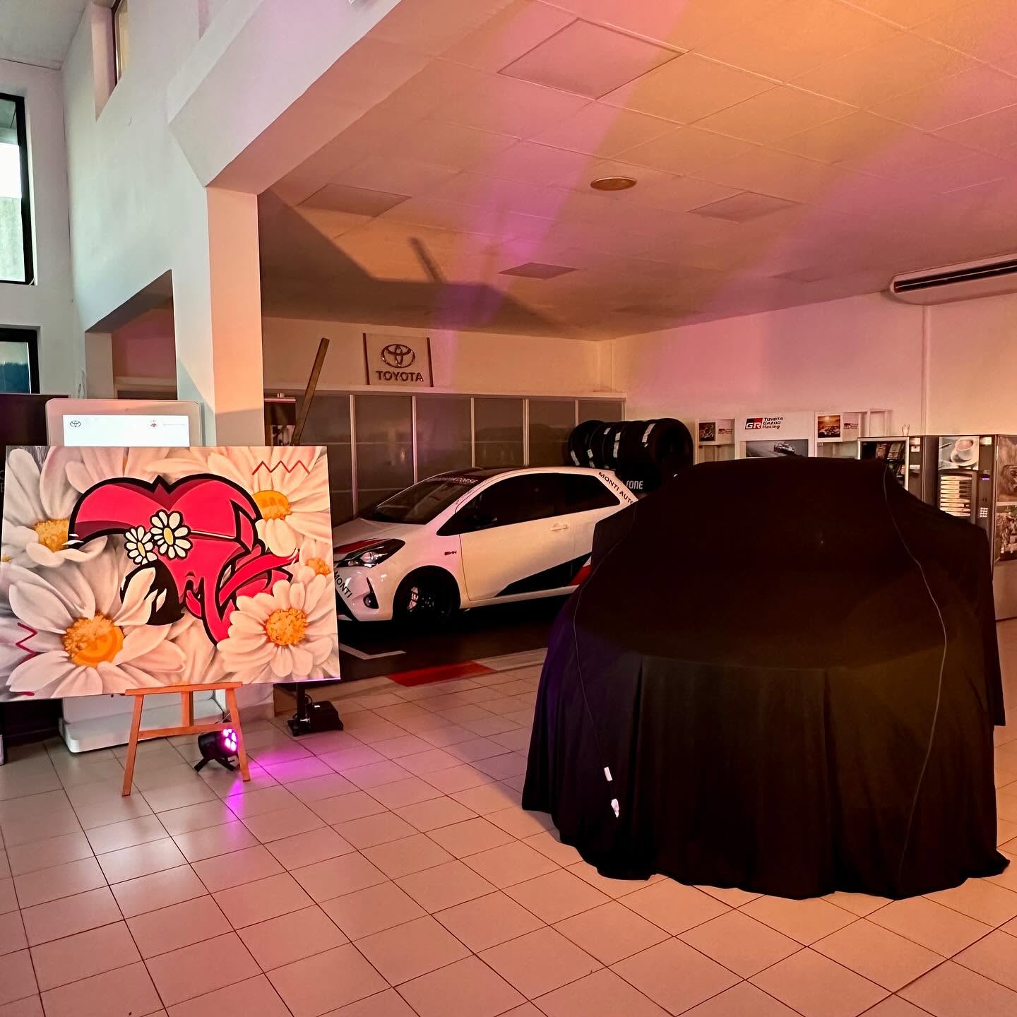 Toile de Hugo W2CJ, cœur rouge entouré de marguerites, exposée dans le hall Toyota près de la voiture sous housse