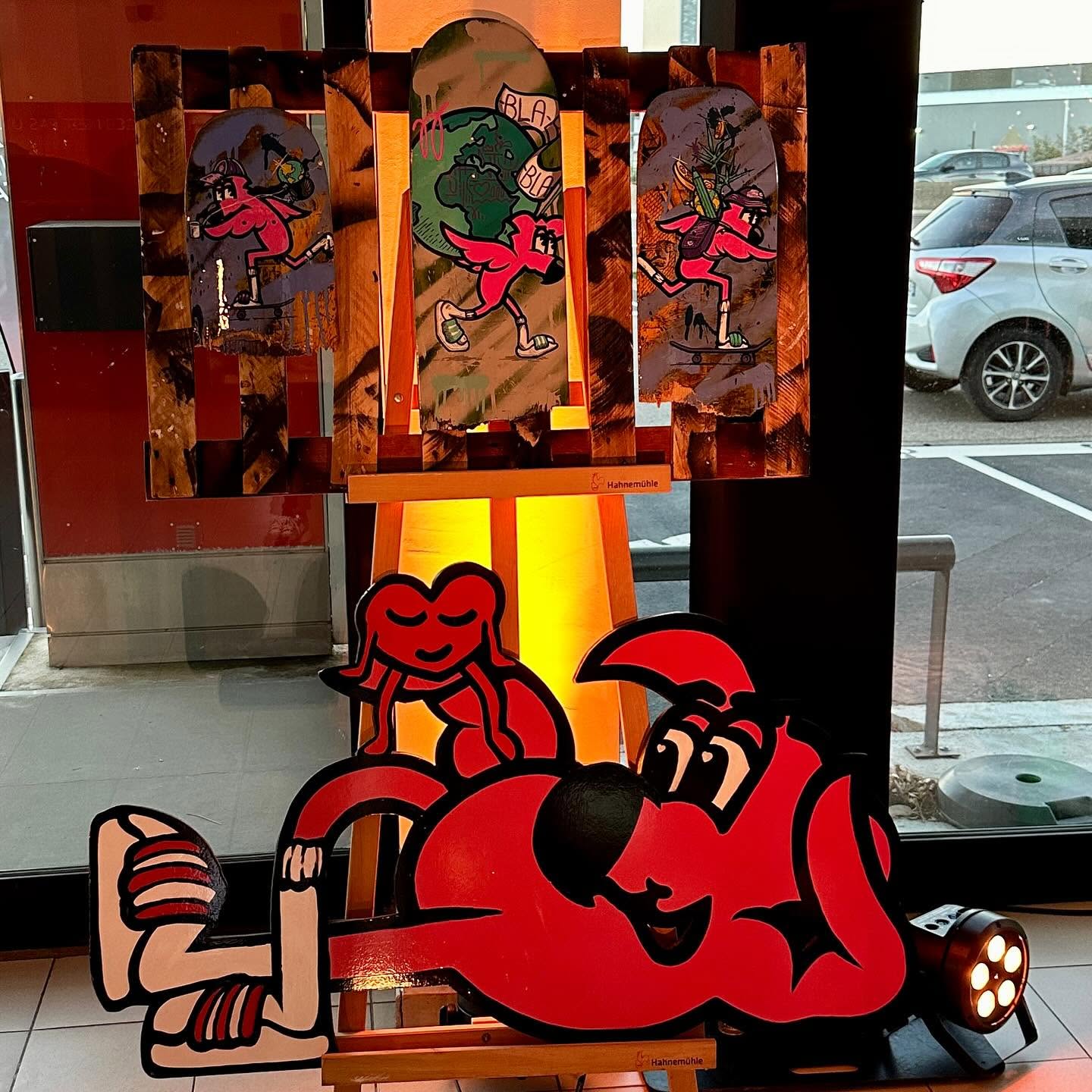 Planches de skate peintes et pièces découpées de Hugo W2CJ exposées dans le hall de la concession