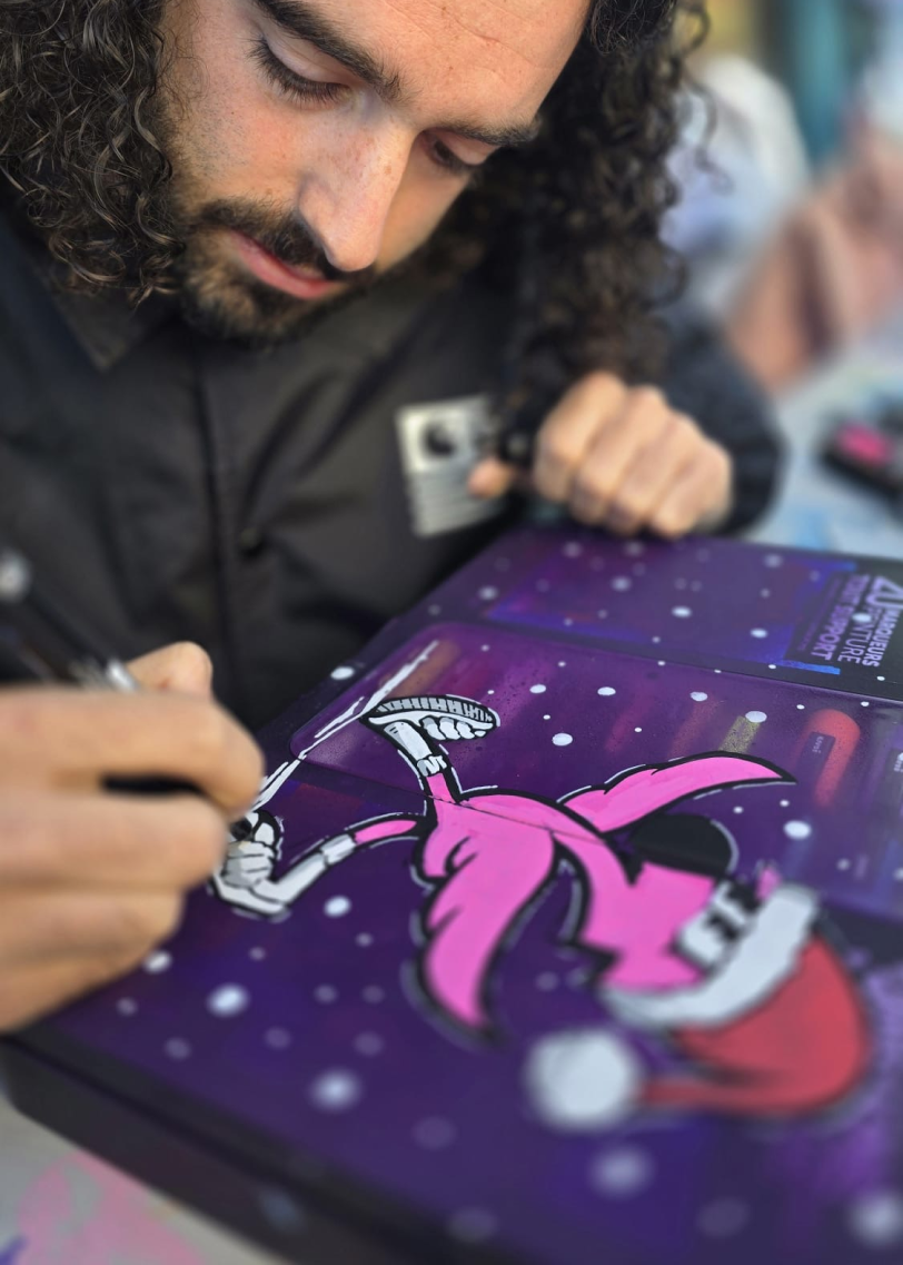 Hugo W2CJ dessine au marqueur Posca sur une mallette violette, un flamant rose en train de skater