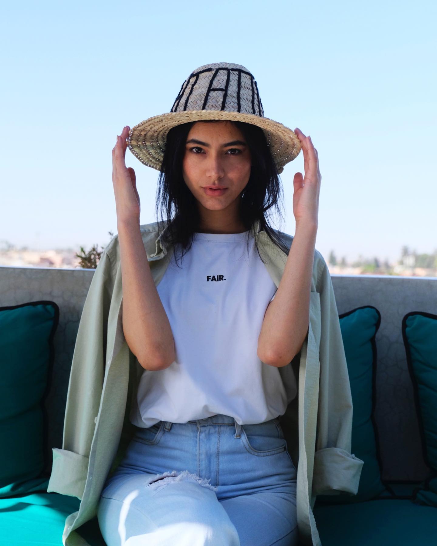 T-shirt Fair blanc porté avec une chemise ouverte, sur une terrasse