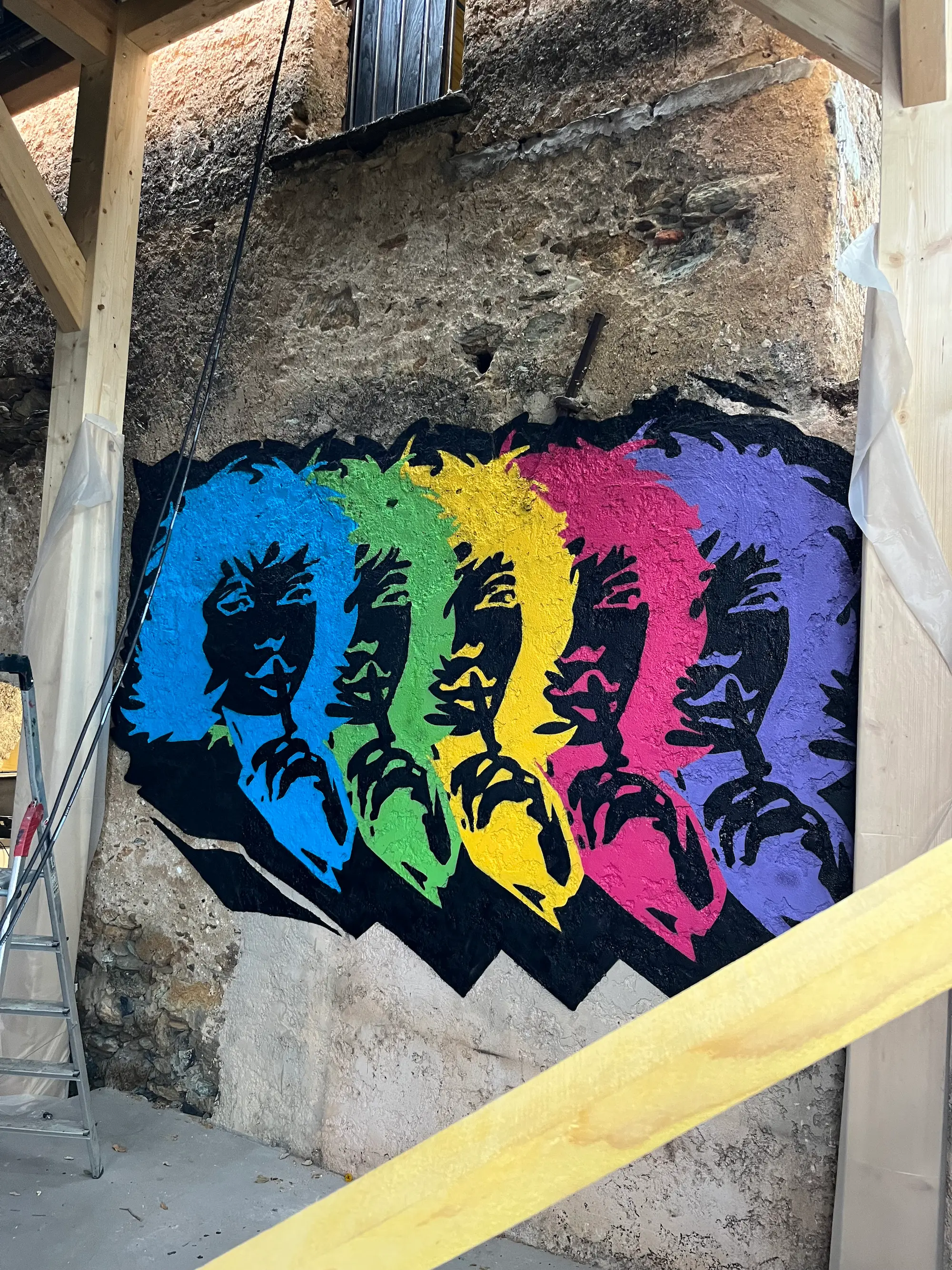 Fresques & décors pour La Conca, fresque, 2020 et 2022 : portrait pop répété en cinq couleurs sur un mur de pierre