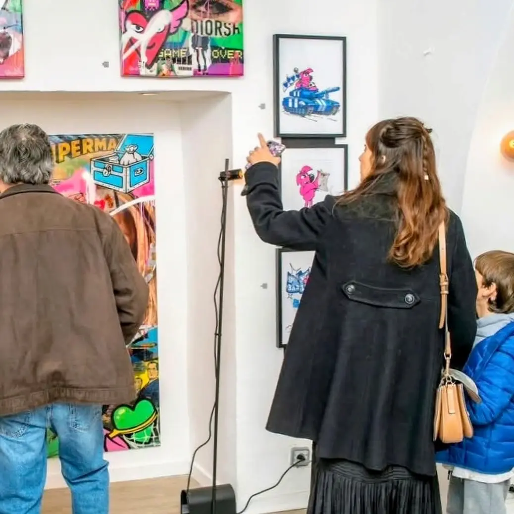 Visiteurs au vernissage de Street Therapy devant une grande toile Superman et des dessins encadrés de Roger le Flamant Rose