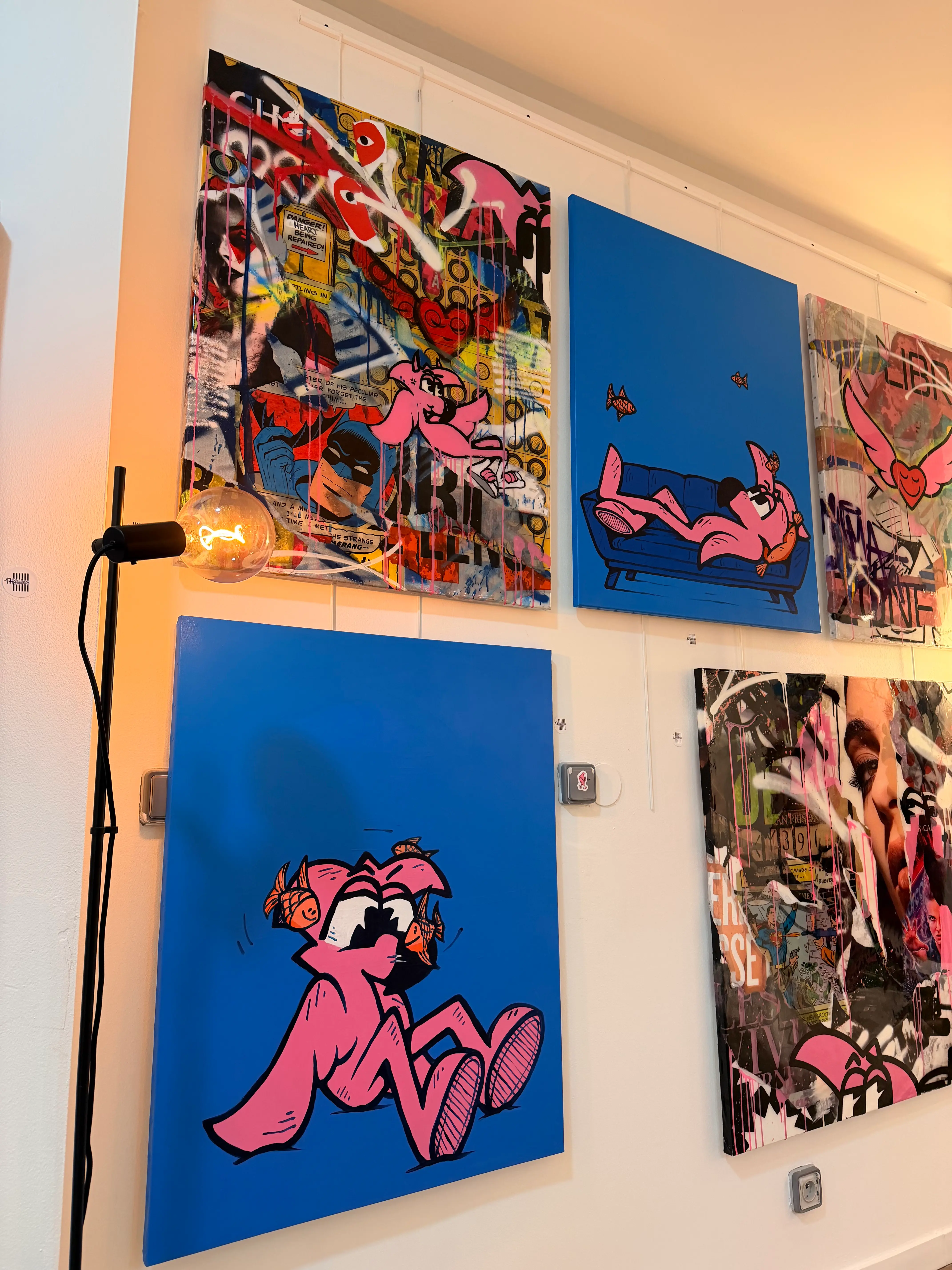 Mur de toiles, dont deux fonds bleus où Roger le Flamant Rose s'allonge sur un canapé et s'assoit entouré de petits poissons