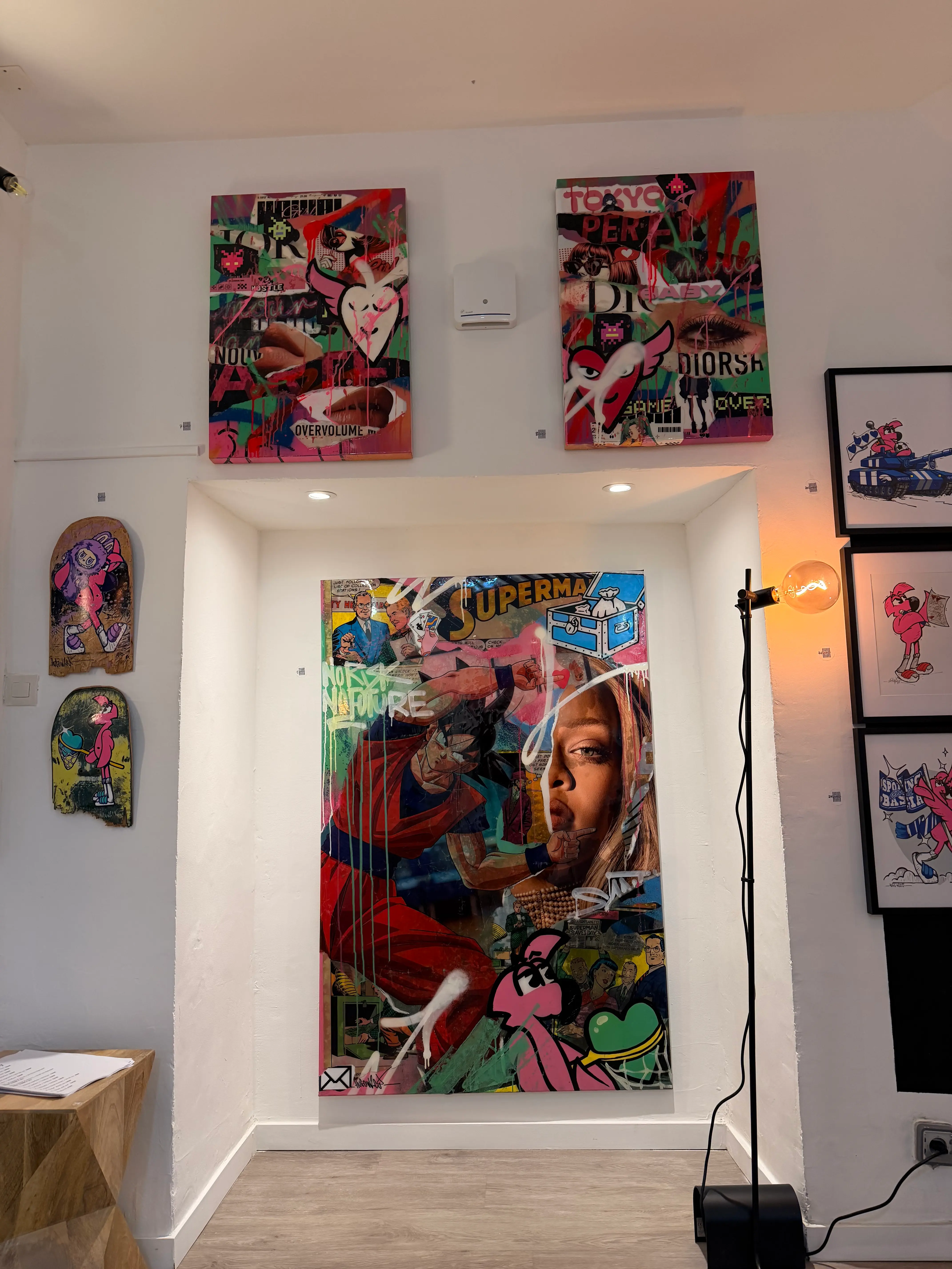 Grande toile Superman en collage et aérosol dans une niche, entourée de deux toiles, de deux planches de skate peintes et de dessins encadrés