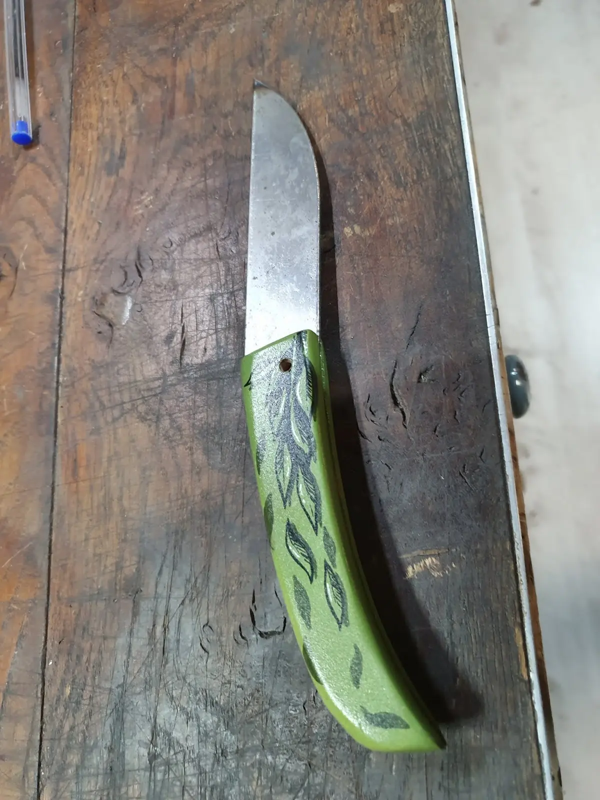 Couteau de Manu Padovani au manche vert peint de feuilles par Hugo W2CJ, posé sur un établi