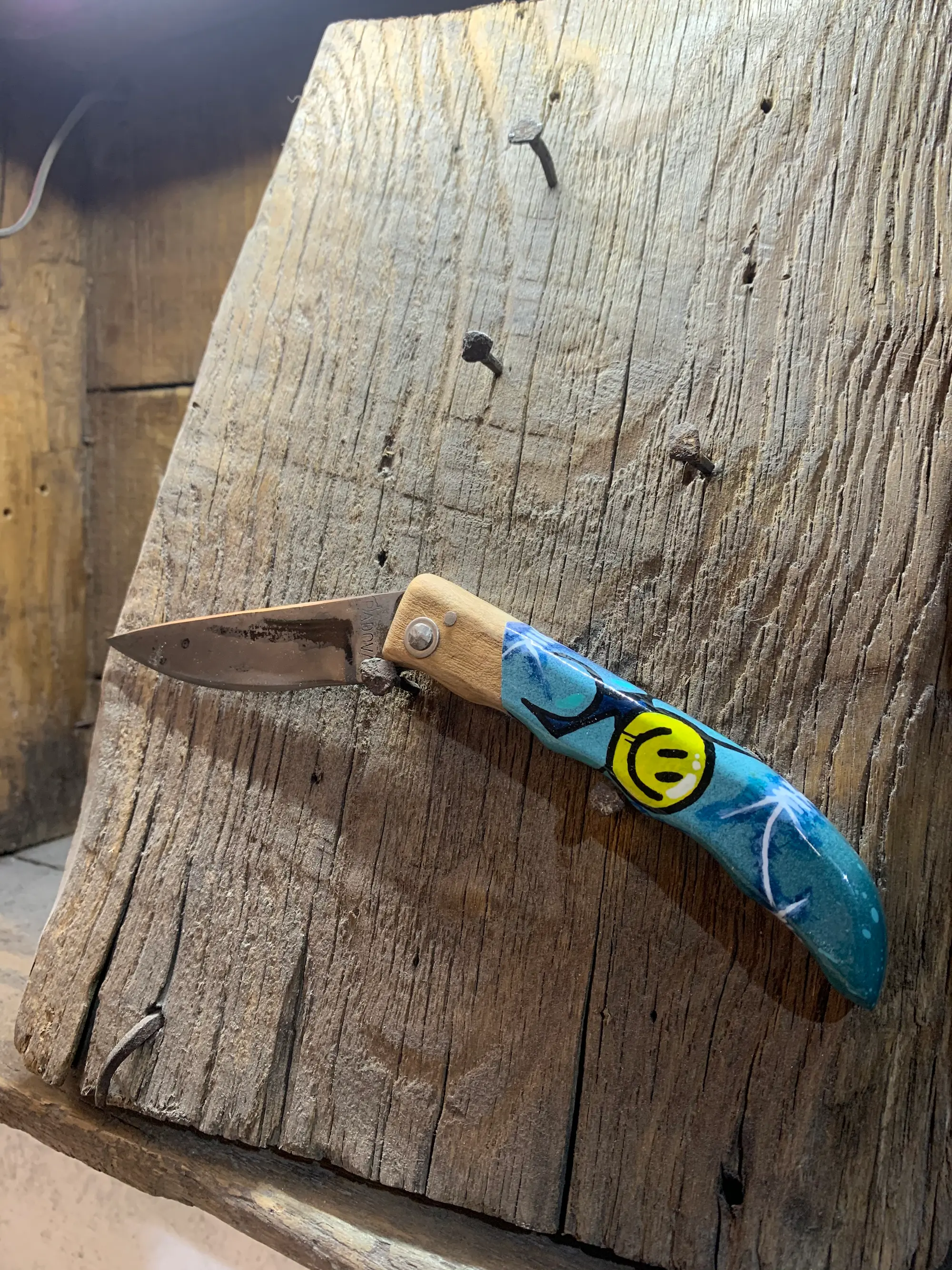 Couteau pliant de Manu Padovani au manche bleu peint par Hugo W2CJ, orné d'un smiley jaune