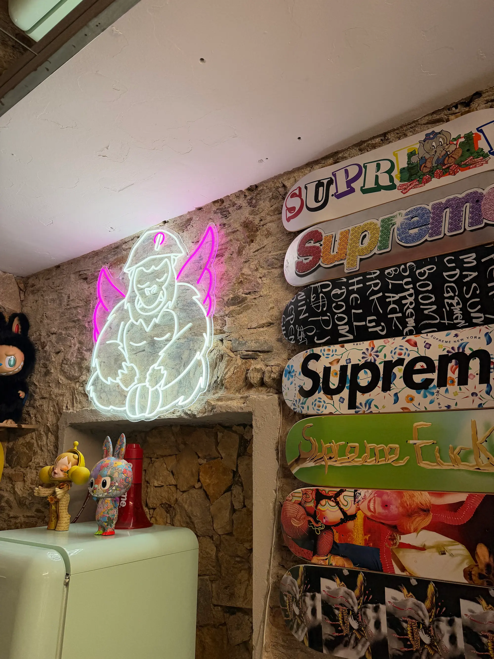 Le néon de la mascotte ailée sur le mur en pierre de Chez Jean, à côté d'une rangée de planches de skate
